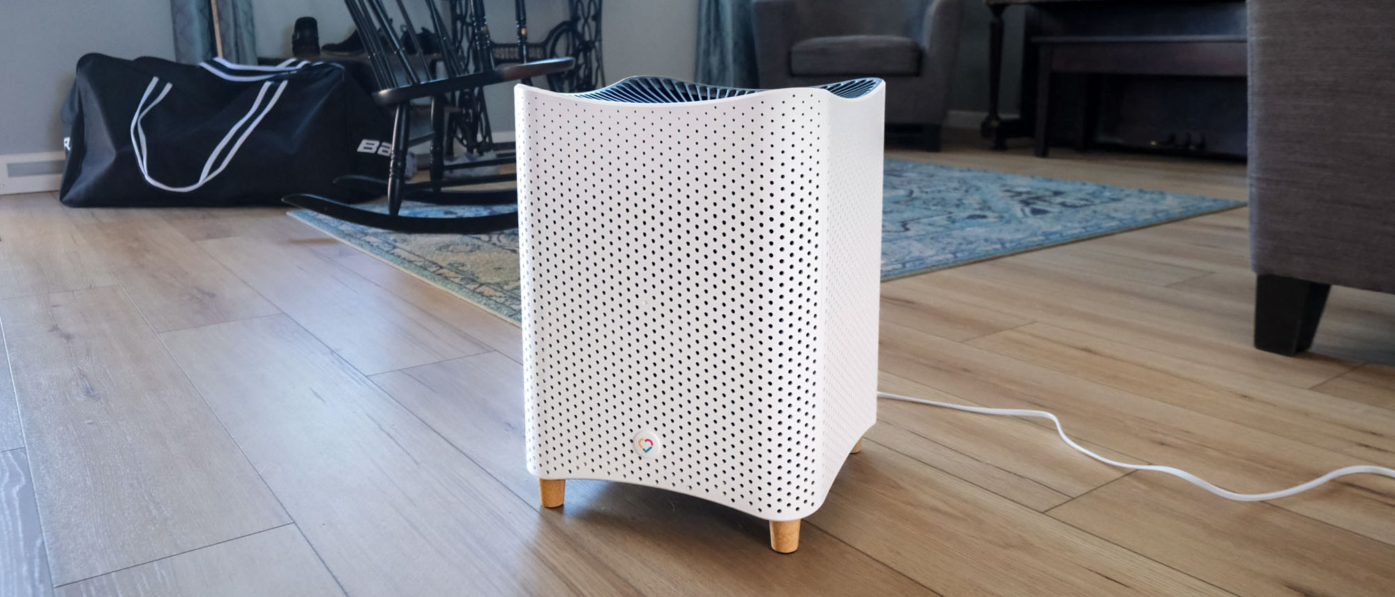 Smart air purifier with a sleek white body and wooden legs placed in a bright, plant-filled living room