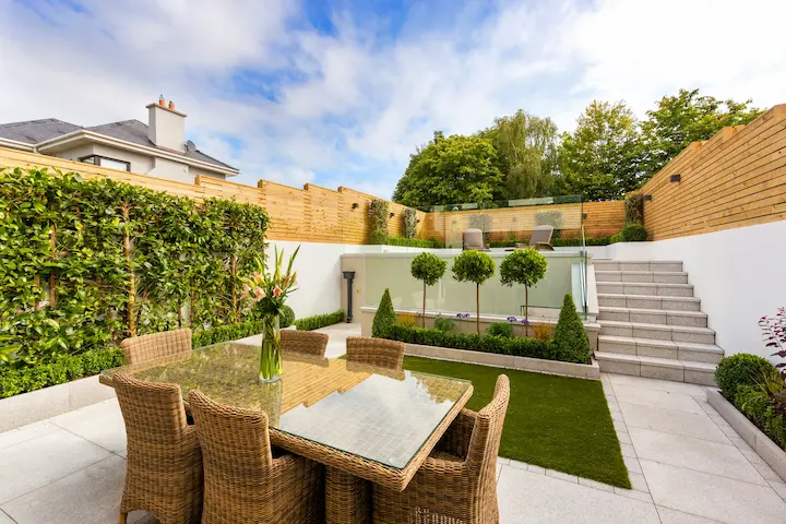 Cozy outdoor patio with round table and chairs next to a wooden fence in sunlight