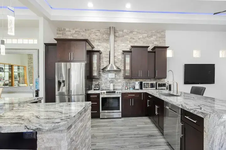 Stainless steel French door refrigerator in a modern white kitchen with marble countertop and smart appliance setup