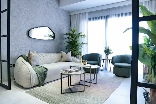 Minimalist living room with cream curved sofa, round mirror, and light wooden furniture.