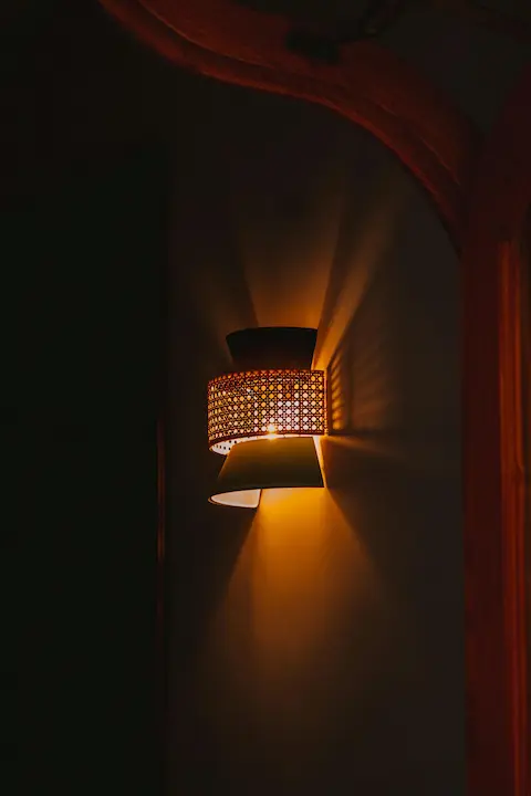 A woven rattan-style wall light glowing warmly in a dark hallway