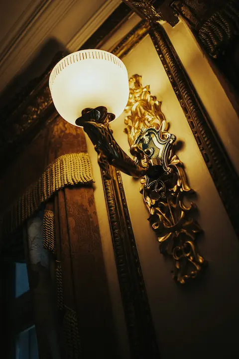 Decorative gold wall sconce with frosted glass shade mounted in a classical luxury room