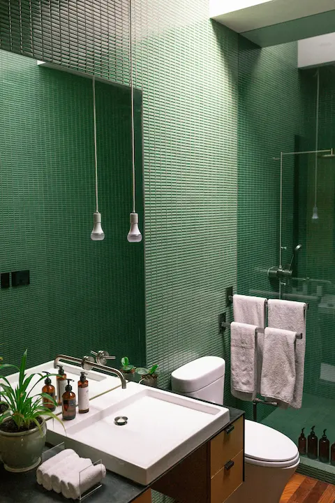 Bathroom with sage green tiled walls, floating white sink, and small potted plant