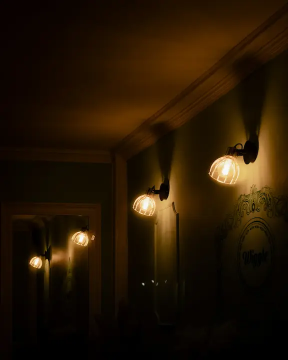 Three cylindrical wall sconces mounted vertically on a hallway wall with warm light