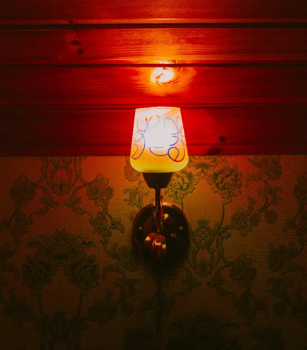 A glowing glass shade wall sconce on vintage wallpapered wall with warm lighting