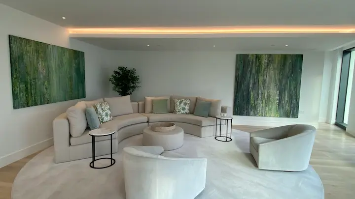 Tranquil monochromatic minimalist living room with curved cream sectional sofa and abstract forest artwork