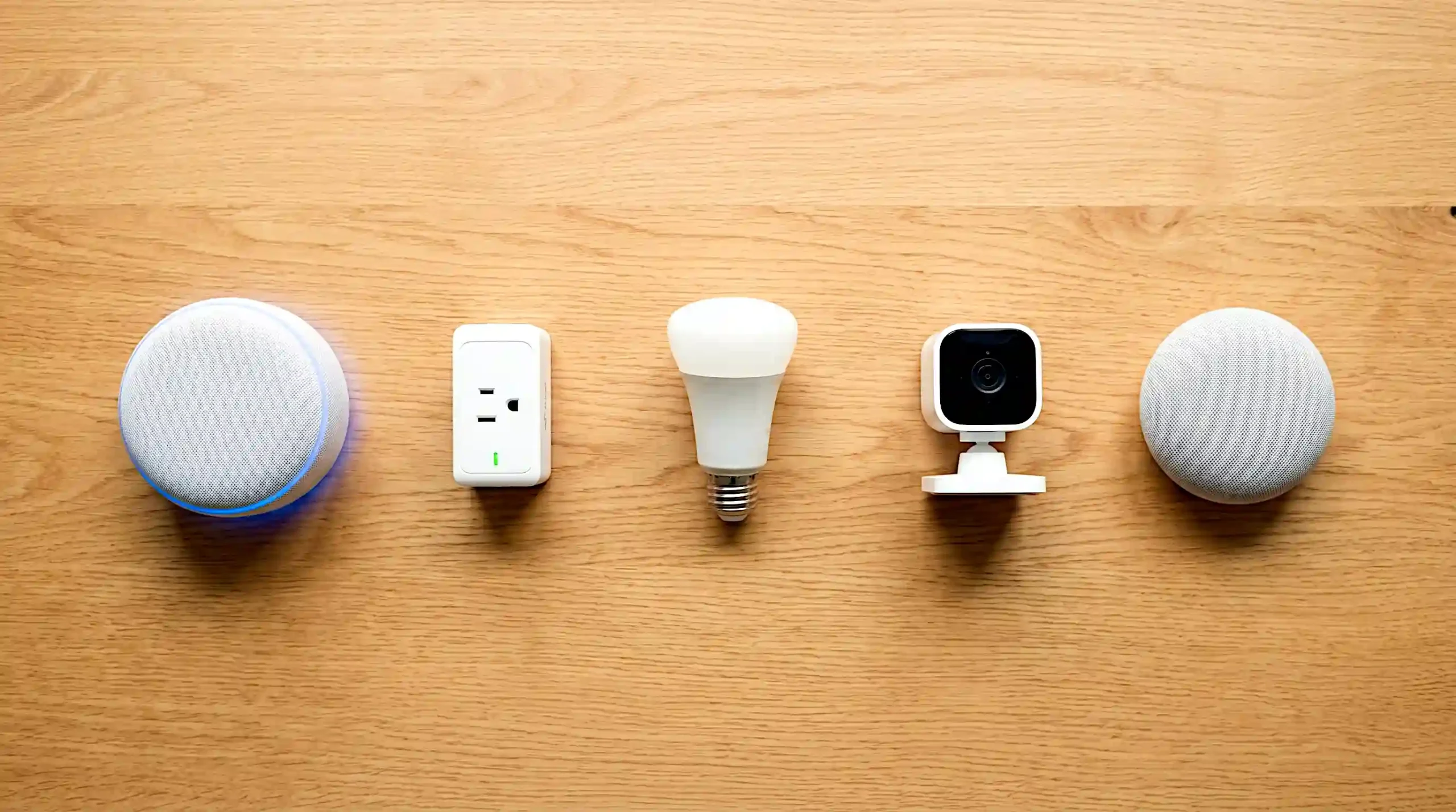 A clean overhead flat-lay of five beginner smart home devices on a warm wood surface including an Echo Dot, smart bulb, small security camera, smart plug, and Google Nest Mini